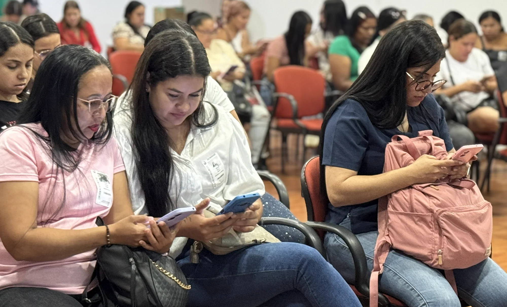 Mujeres emprendedoras practicando con sus teléfonos durante un taller en un auditorio.